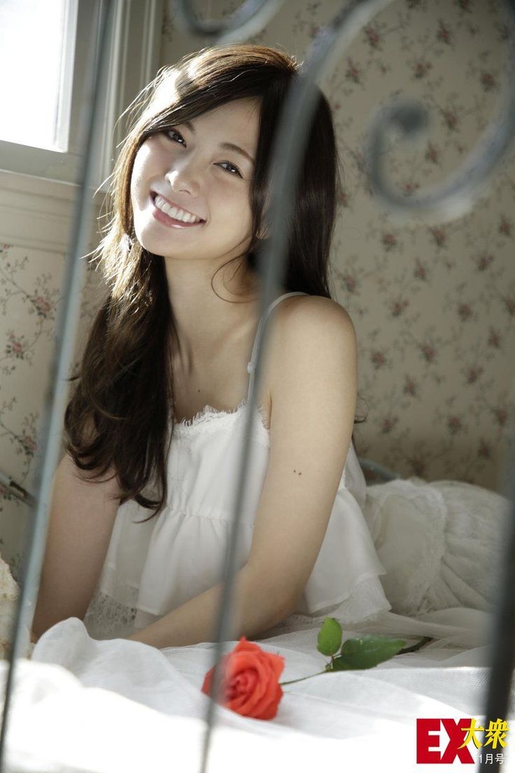 Smiling woman with long hair in a white dress in a sunlit bedroom