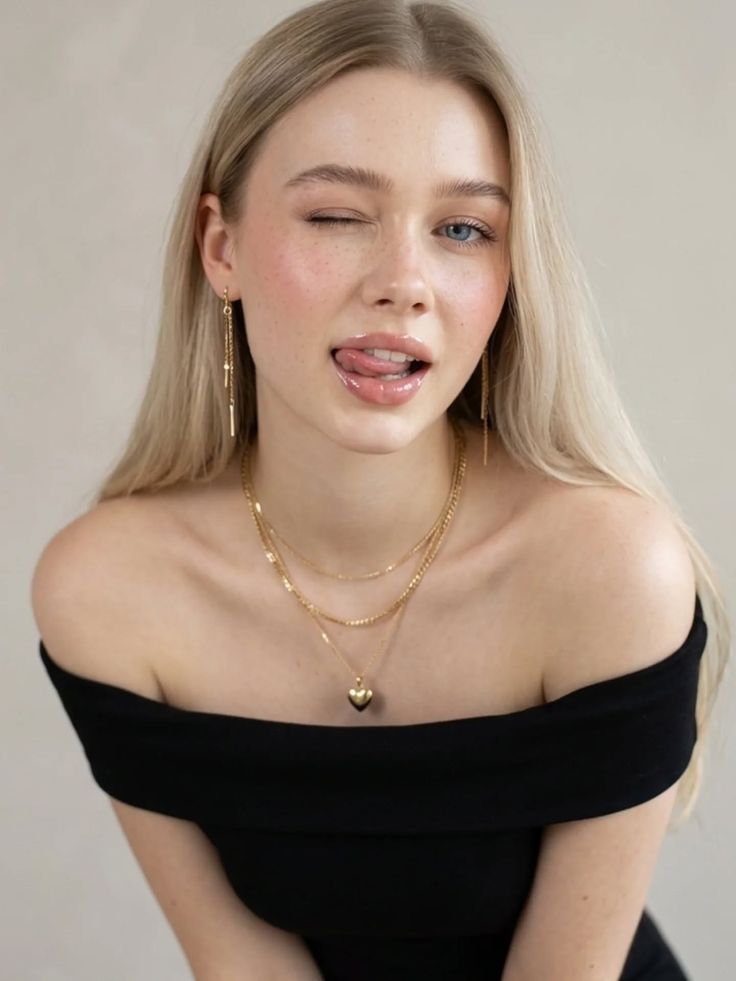 Blonde woman winking with her tongue out, wearing an off-shoulder top and gold jewelry