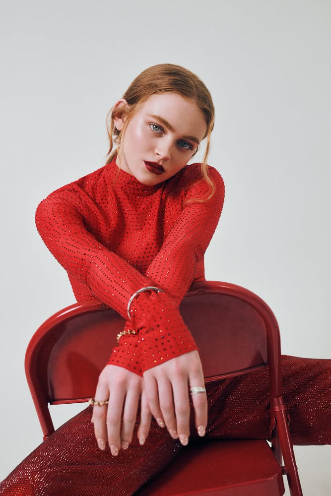 Woman with red hair and red lipstick wearing a red top with embellishments