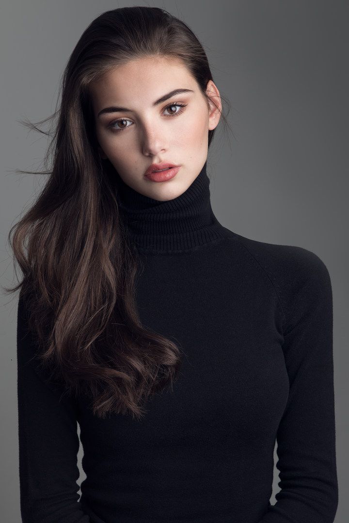 Woman with long dark hair wearing a black turtleneck in a studio setting