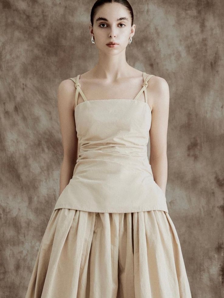 Woman in a beige sleeveless top and pleated skirt in a studio setting