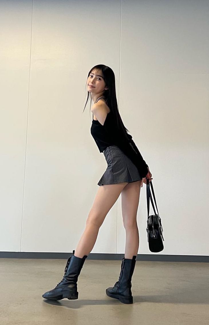 Woman with long black hair in a mini skirt and combat boots posing indoors