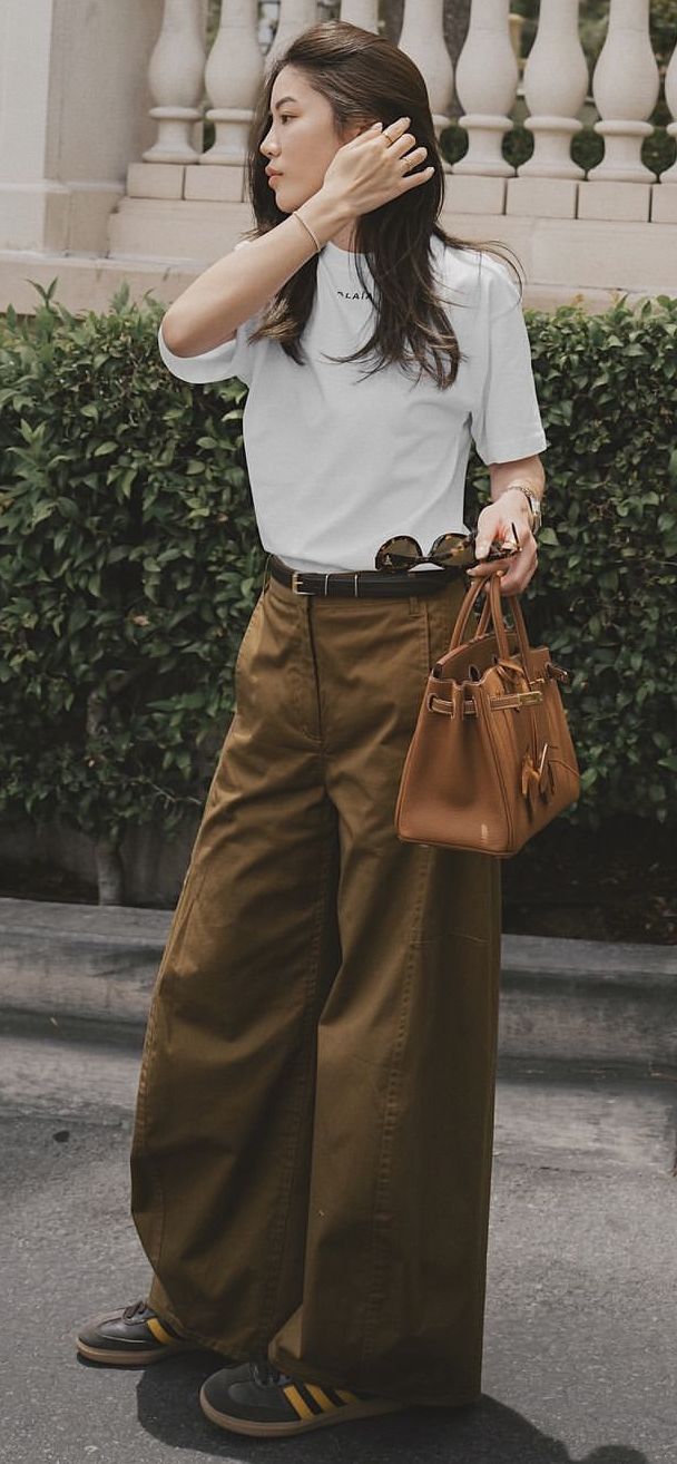 Woman in a white t-shirt and wide leg pants holding a brown handbag outdoors