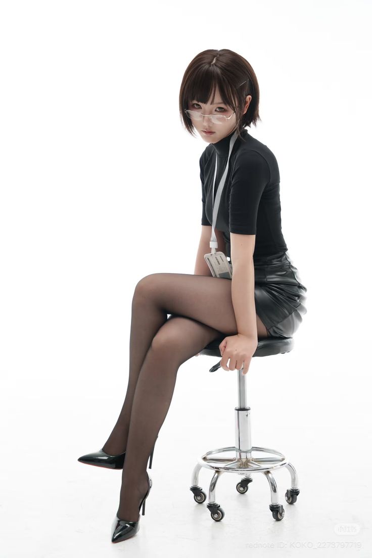 Woman with short hair and glasses wearing a black turtleneck and leather skirt