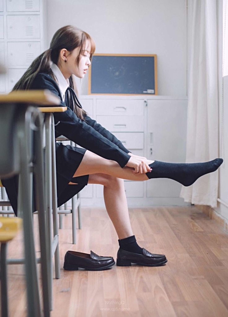 Girl in a school uniform putting on socks in a classroom