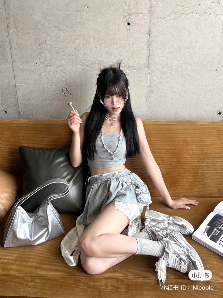 Woman with long black hair wearing a crop top and mini skirt, sitting on a couch