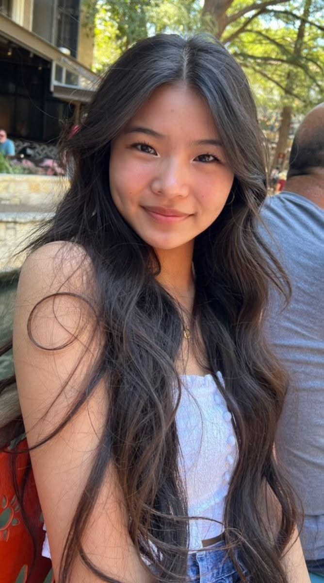 Young woman with long dark hair smiling outdoors in daylight