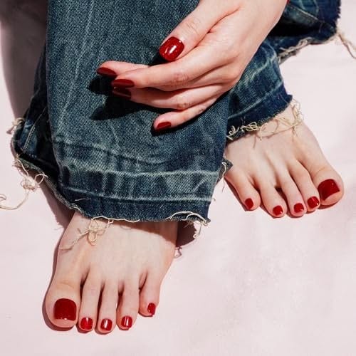 Hands and feet with red nail polish, wearing ripped denim jeans