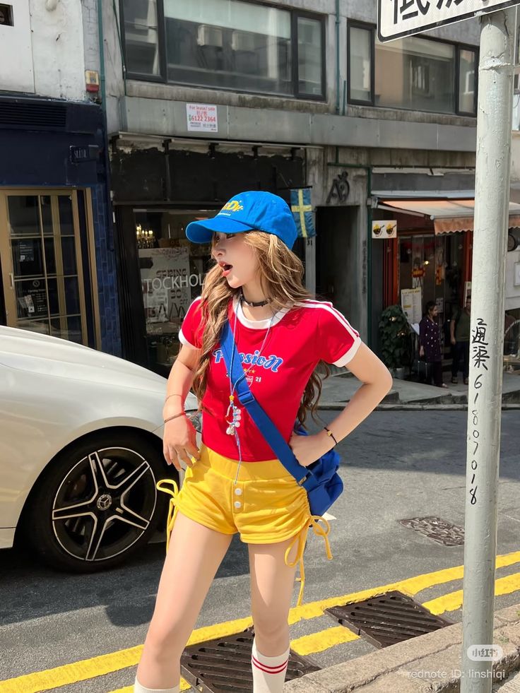 Woman in a blue cap, red t-shirt, and yellow shorts on a city street