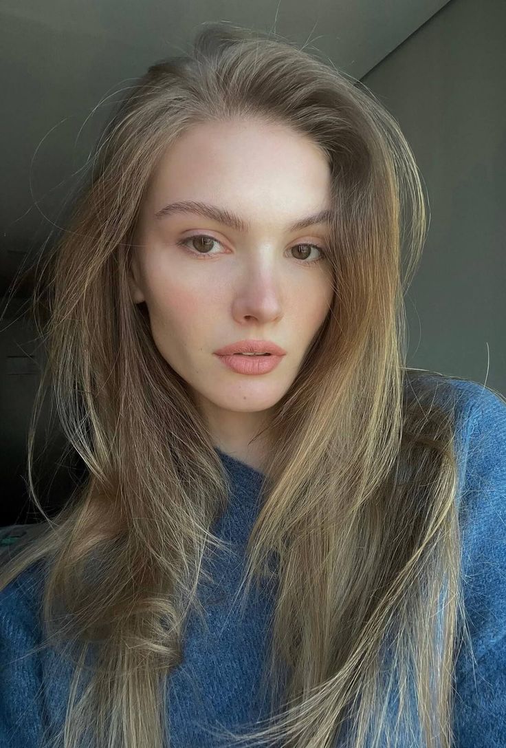 Woman with long blonde hair wearing a blue sweater, captured in soft lighting