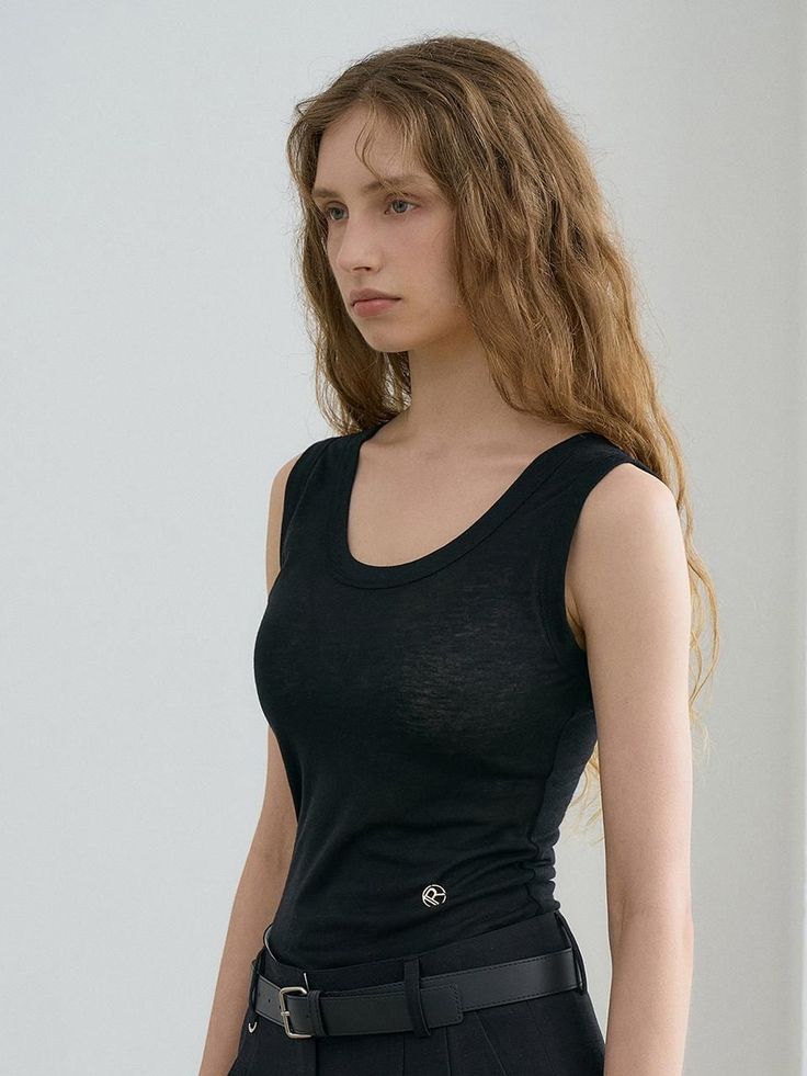 Woman with long hair wearing a black tank top and belt against a white background