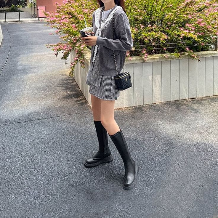 Person in a gray cardigan and plaid skirt with knee-high boots outdoors