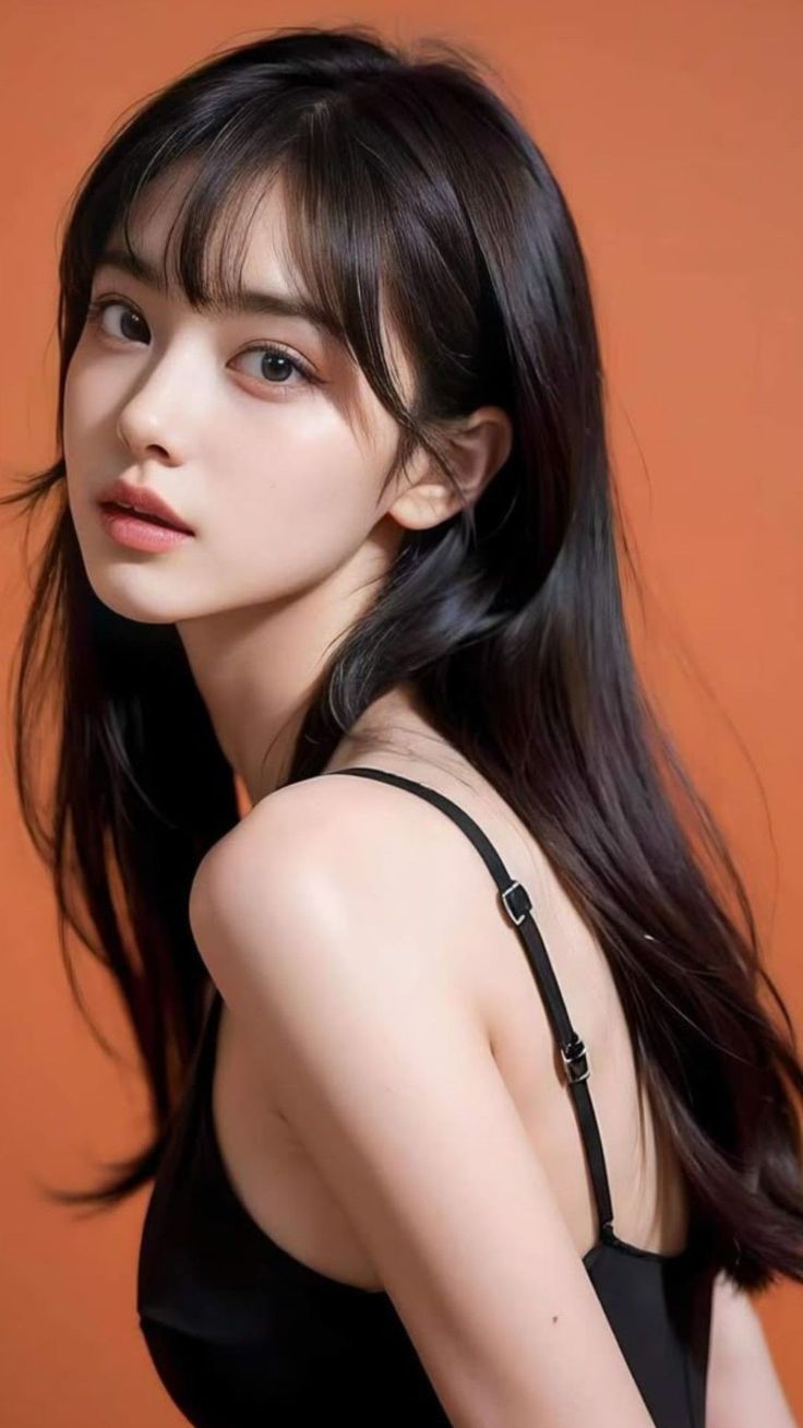 Woman with long black hair wearing a black top against an orange background