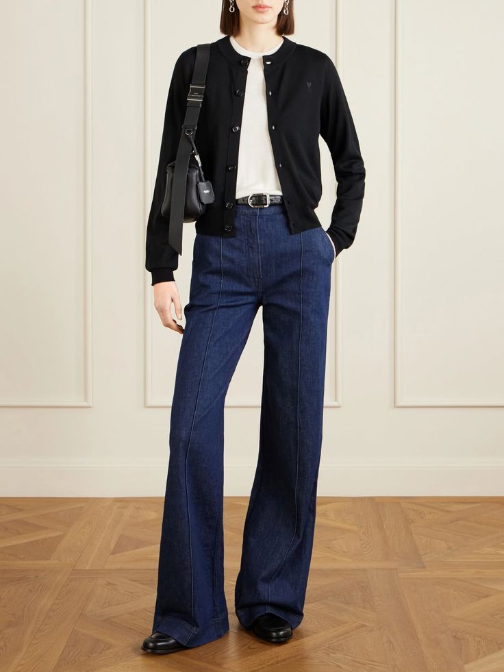 Woman in a black cardigan and wide leg jeans standing indoors