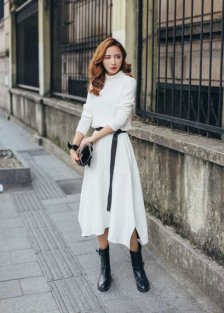 Woman in a white dress with a black belt and boots standing on a street
