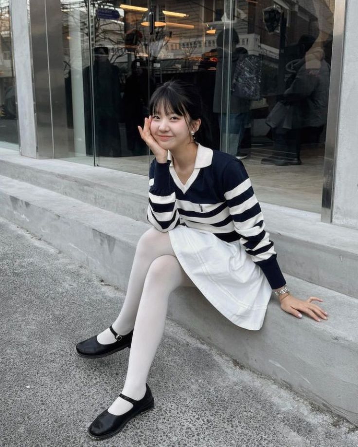 Woman in a striped sweater and white skirt sitting on concrete steps outdoors