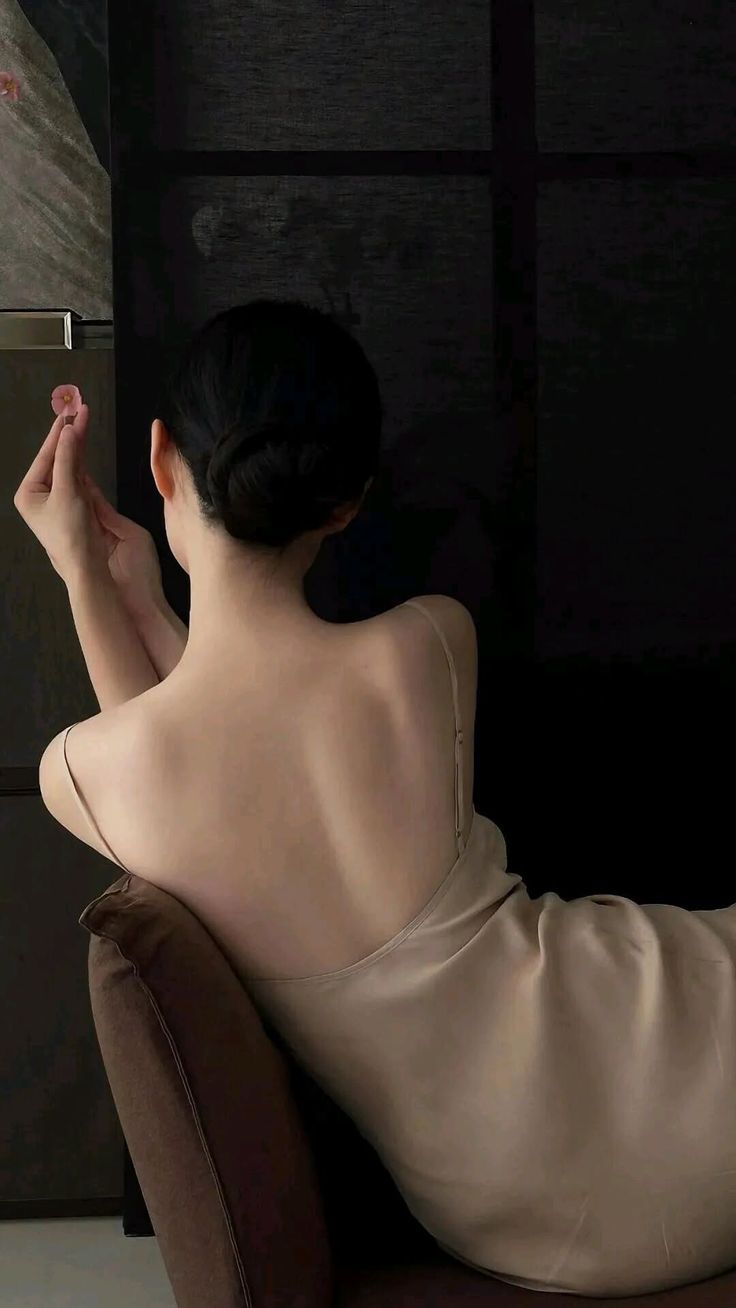 Woman with bare back and updo in a slip dress, holding a small flower