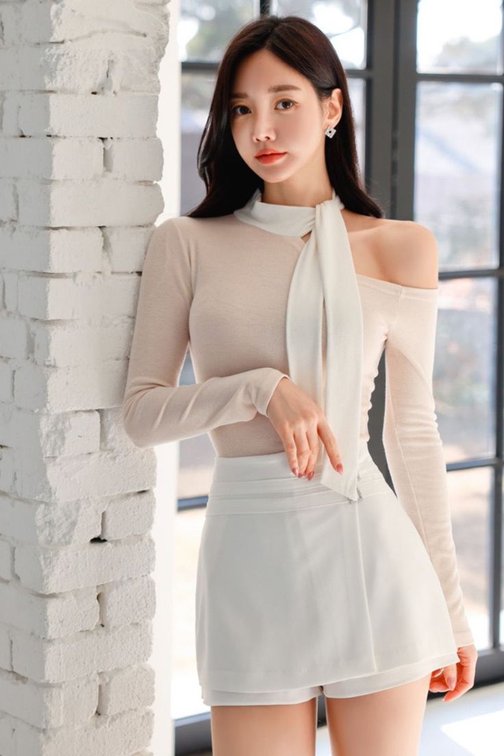 Woman with long dark hair wearing an off-shoulder top and white skirt indoors