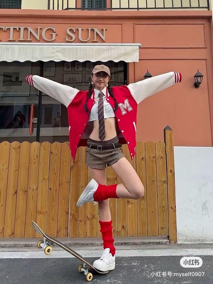 Woman in a varsity jacket, crop top, and plaid shorts posing with a skateboard
