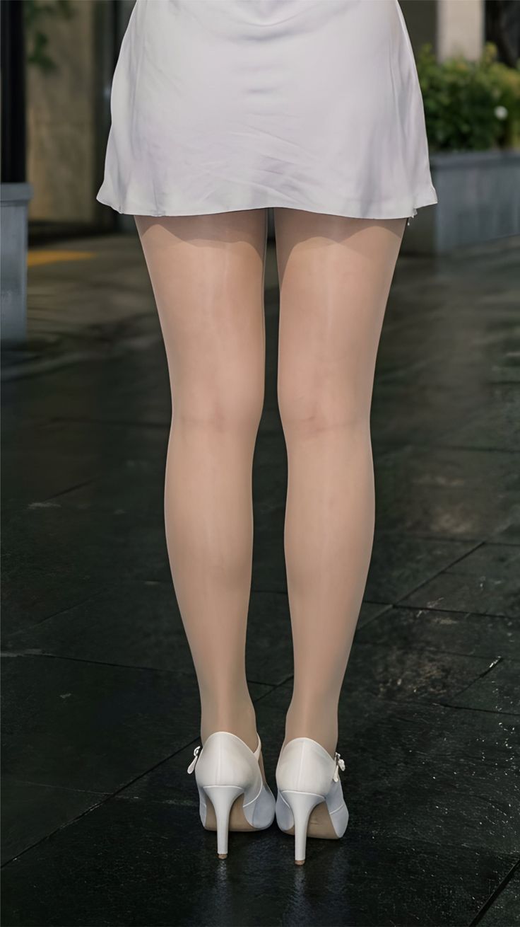 Person in a white skirt, pantyhose, and white high heels standing outdoors