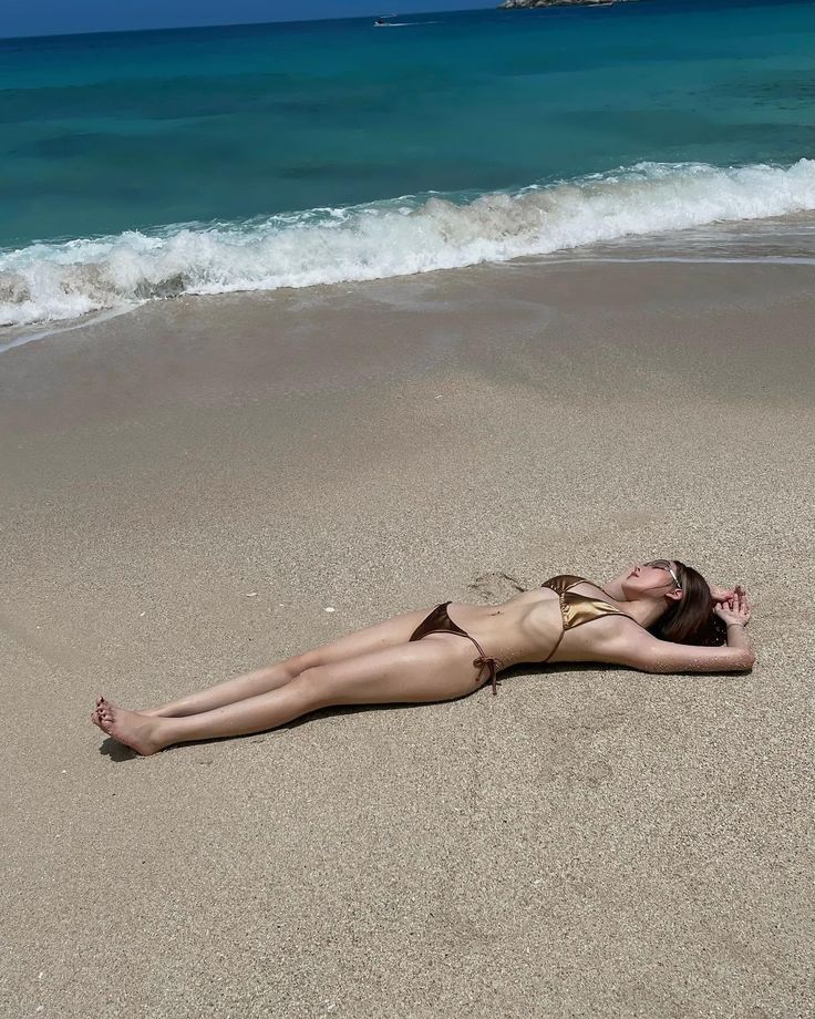 Woman in a bikini lying on a sandy beach with waves in the background
