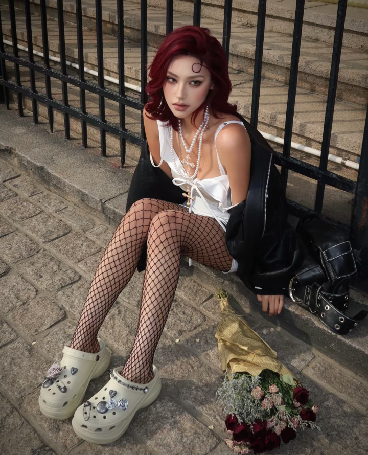 Woman with red hair and fishnet stockings sitting on a stone ground with roses