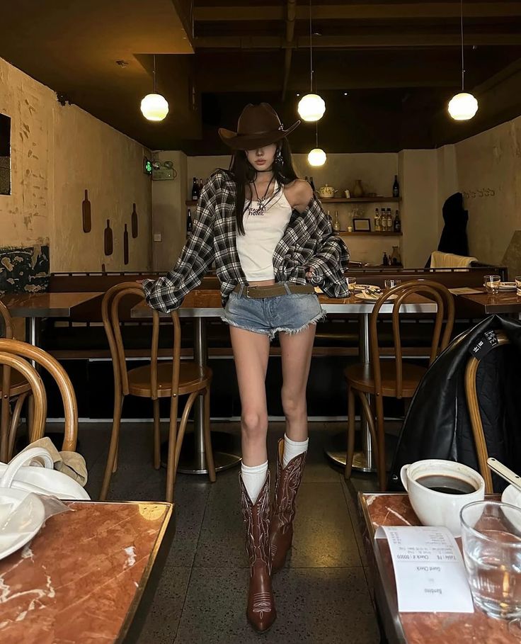 Woman in a cowboy hat, plaid shirt, and denim shorts in an indoor setting