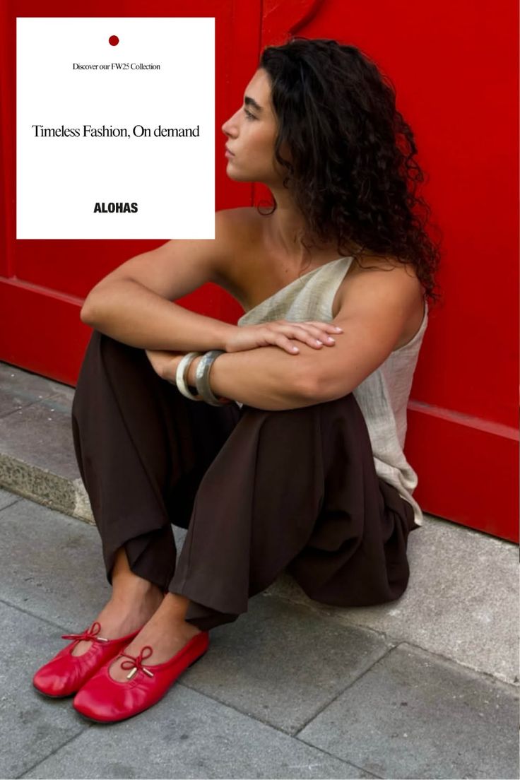 Woman with curly hair sitting on a sidewalk against a red background