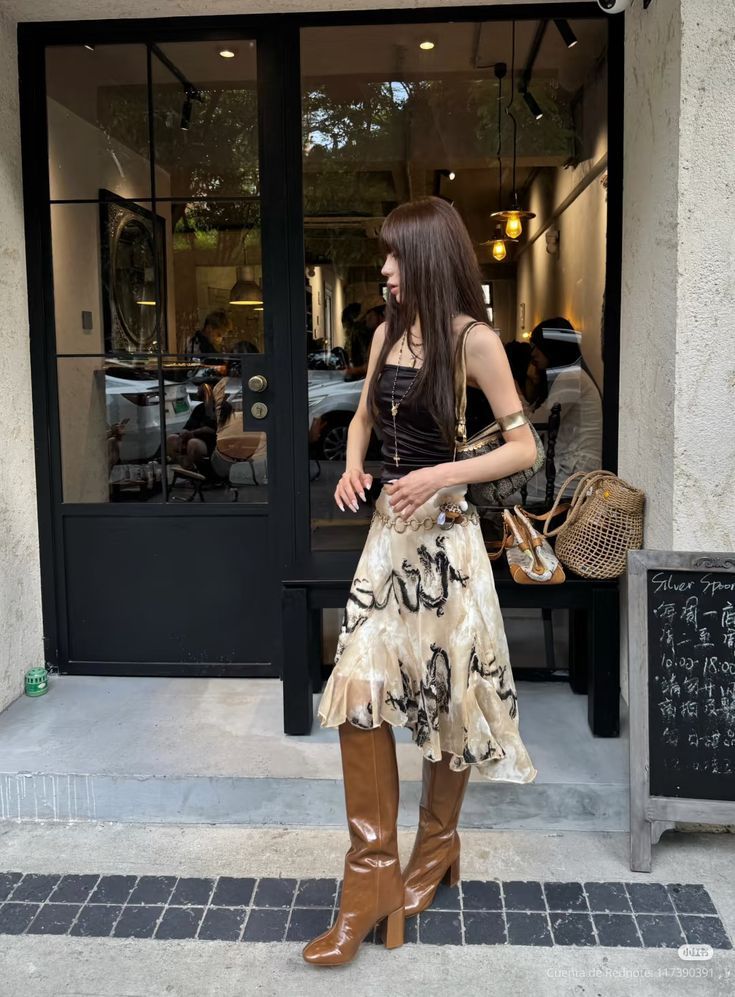 Woman in a strapless top, midi skirt, and brown boots standing outside a cafe