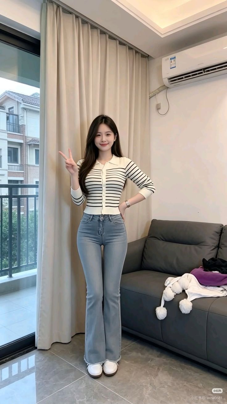 Woman with long hair wearing a striped top and flared jeans, posing indoors