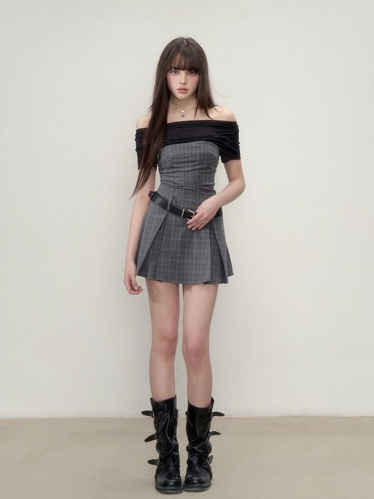 Woman in an off-shoulder top and plaid skirt with black boots standing indoors