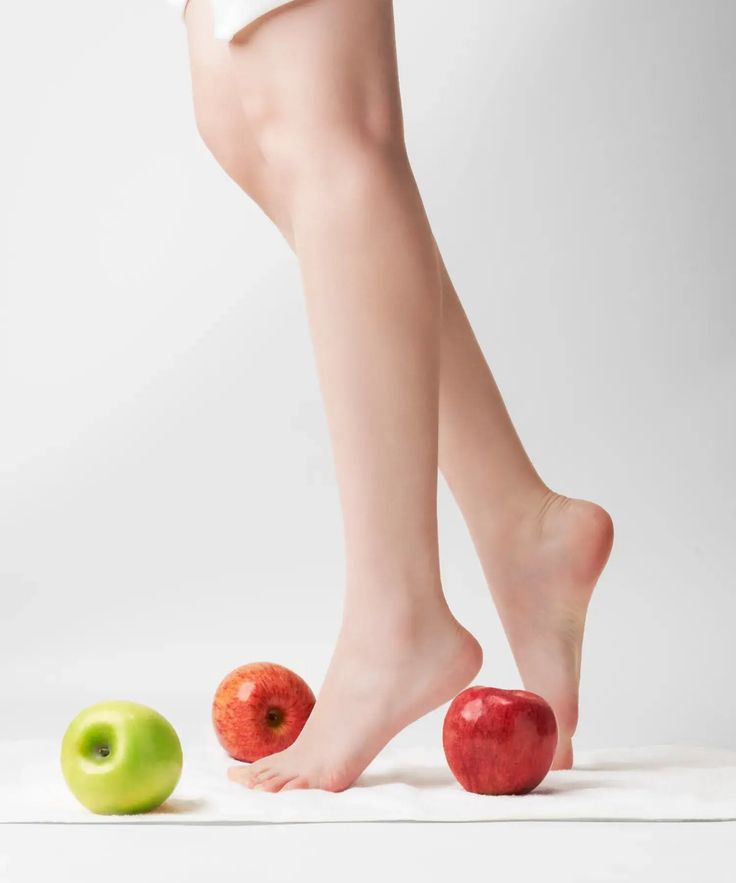 Bare legs and feet with red and green apples on a white surface