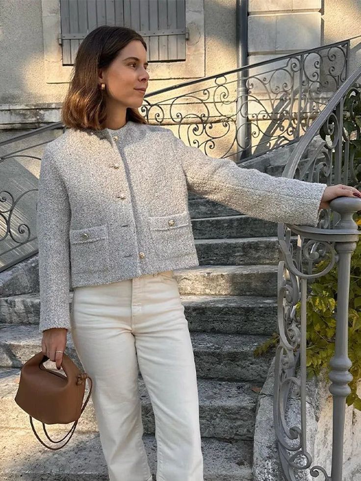 Woman in a tweed jacket and white pants holding a brown handbag on outdoor stairs