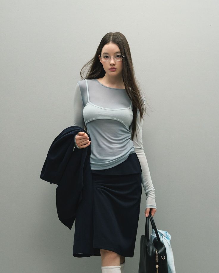 Woman with long hair and glasses wearing a sheer top and dark skirt