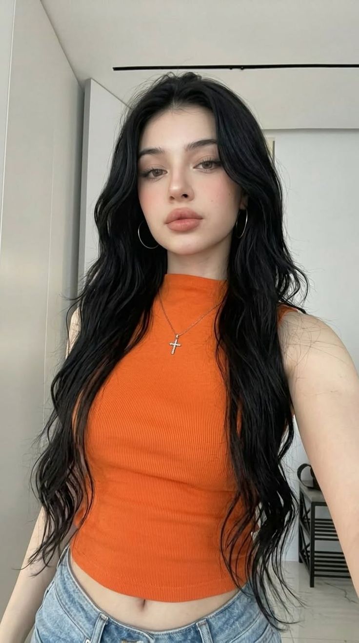 Woman with long black hair wearing an orange top and jeans indoors