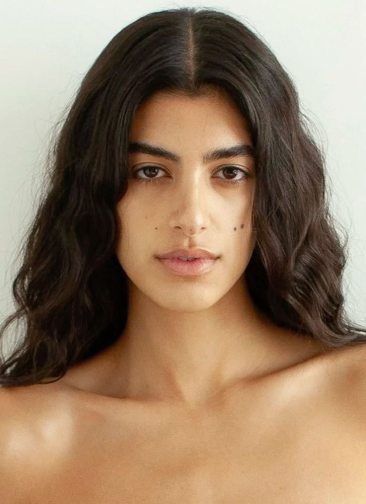 Woman with long dark wavy hair and bare shoulders looking directly at the camera