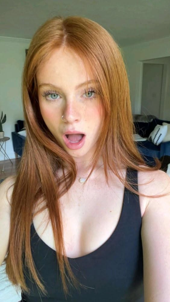 Woman with long red hair and green eyes wearing a black tank top indoors