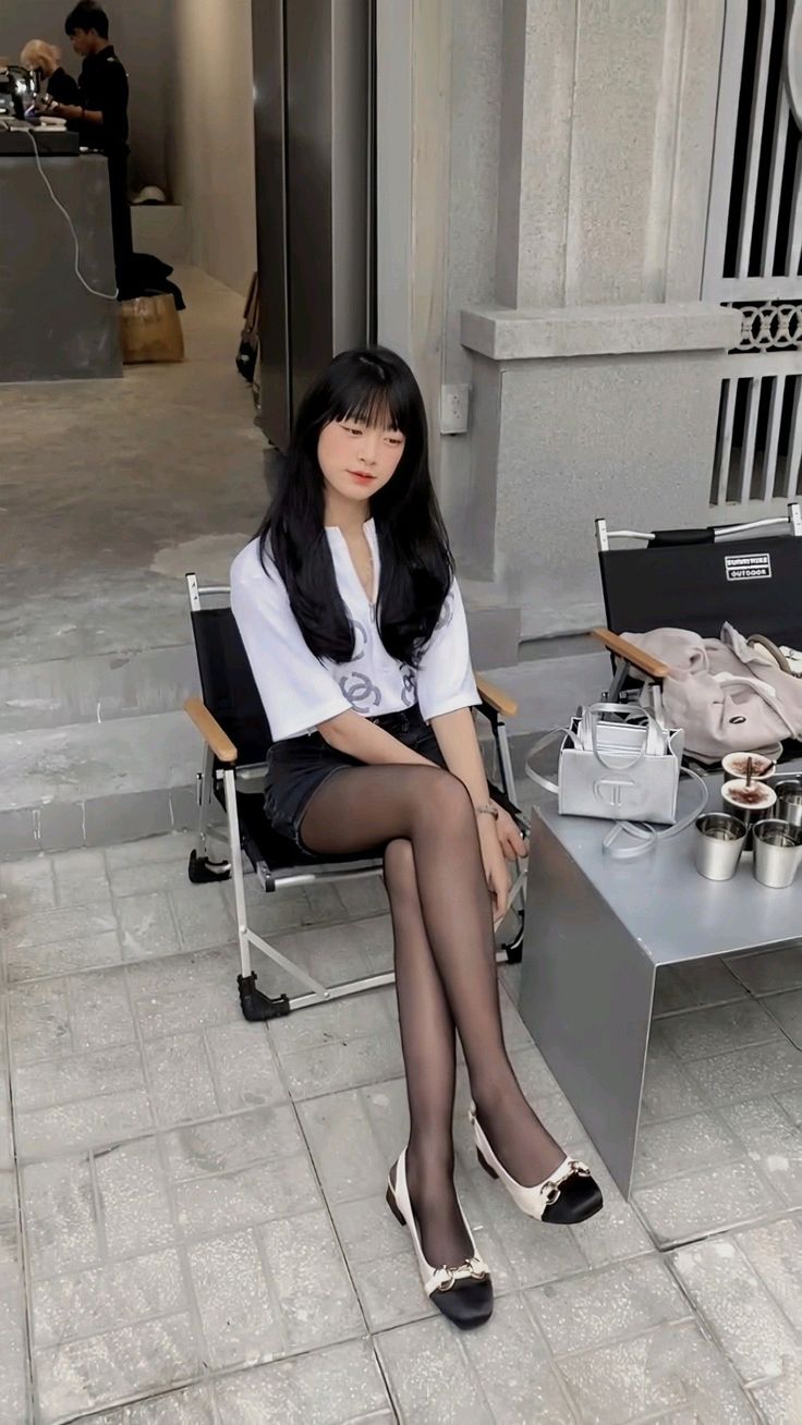 Woman with long black hair sitting outdoors in a white shirt and black shorts