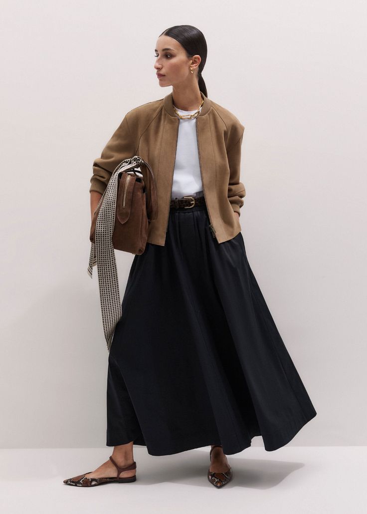 Woman in a brown bomber jacket and black maxi skirt holding a brown handbag