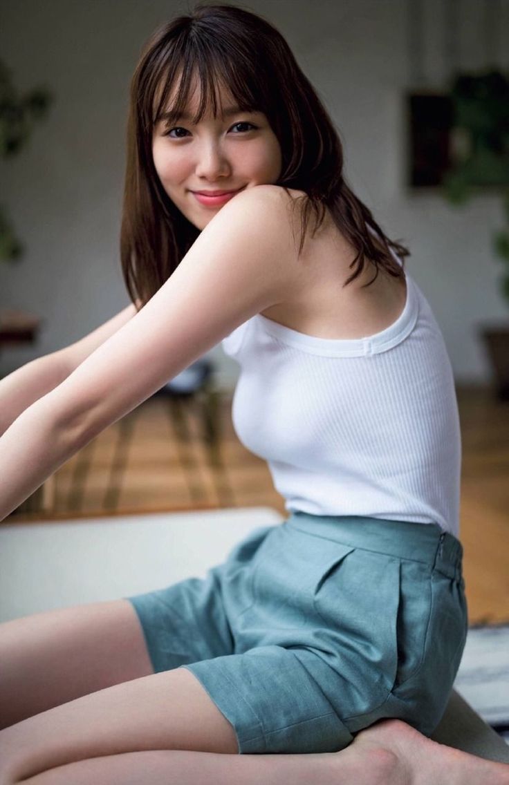 Woman in a white tank top and green shorts smiling indoors