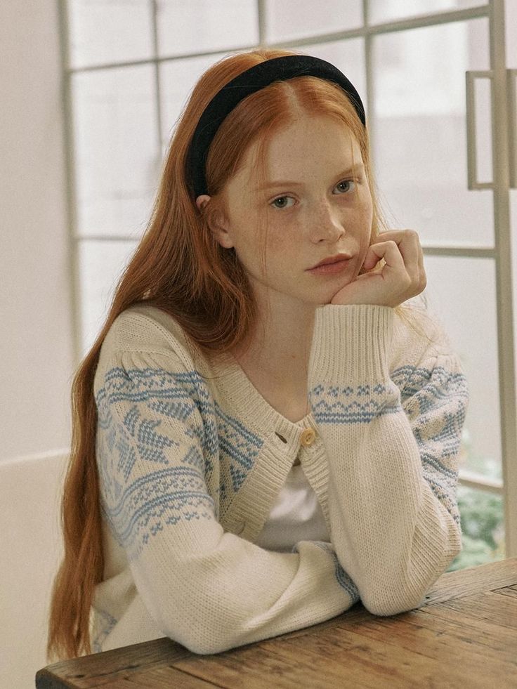 Young woman with red hair and freckles wearing a cardigan, resting her chin on her hand