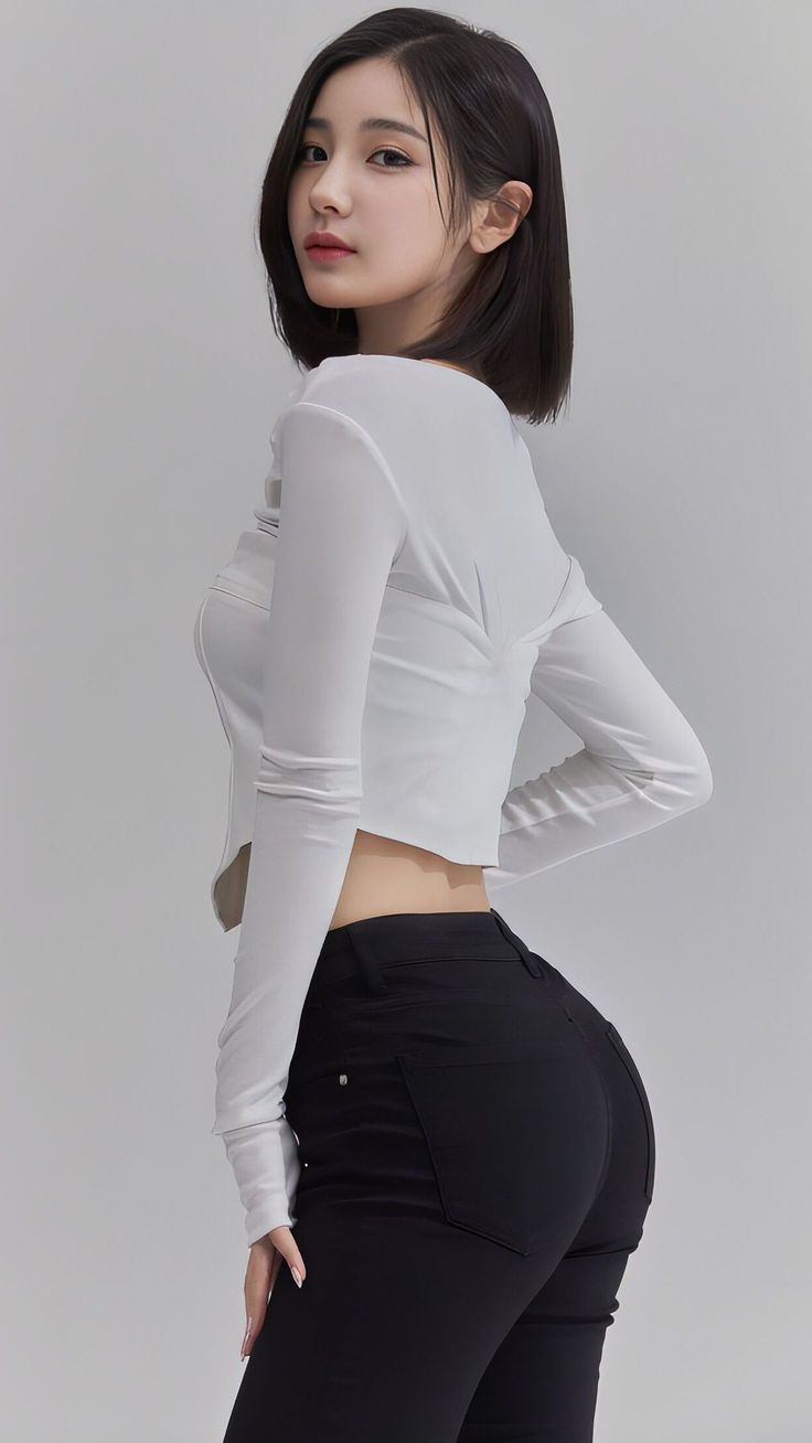 Woman with short black hair in a white crop top and black pants posing indoors