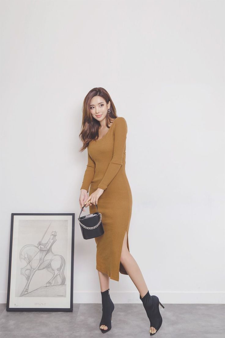 Woman in a brown dress and black boots holding a small handbag indoors