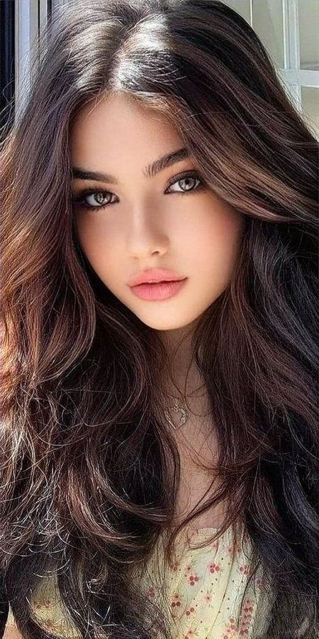 Woman with long wavy brown hair and pink lips wearing a heart necklace