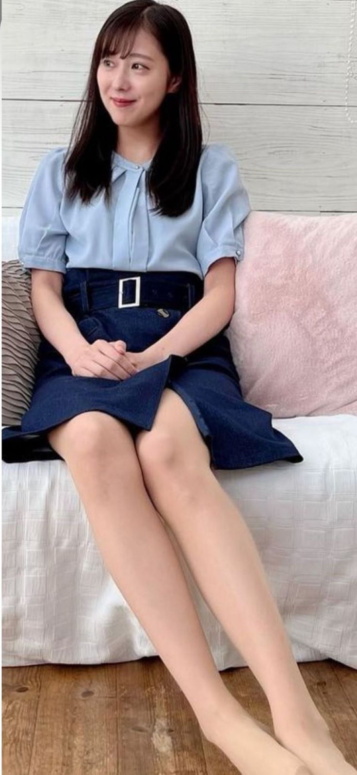 Woman with long dark hair wearing a blue blouse and denim skirt, sitting indoors