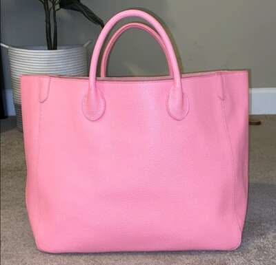 Pink leather tote bag with top handles on a textured floor indoors