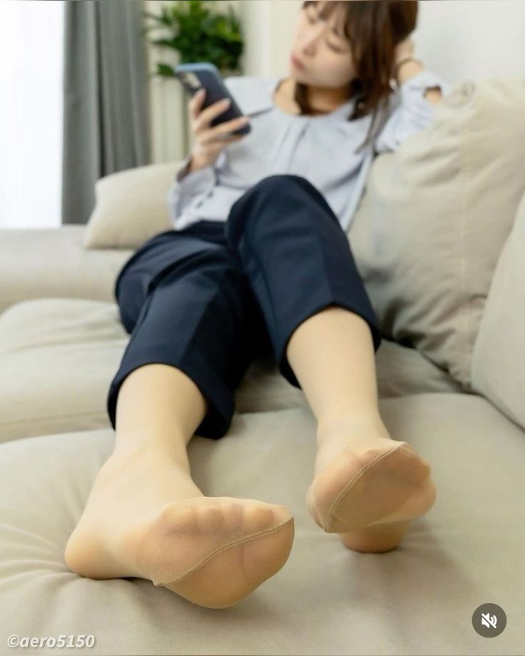 Woman relaxing on a couch, wearing nude pantyhose and using a phone