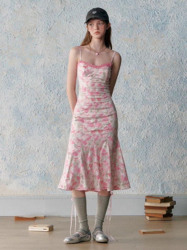 Young woman in a pink floral dress and baseball cap standing indoors