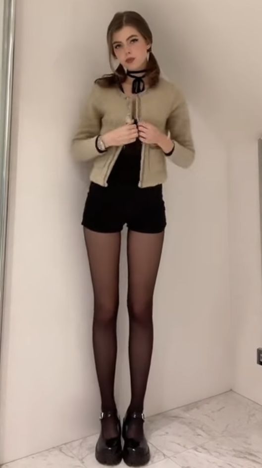Woman with pigtails wearing a cardigan, black shorts, and tights indoors