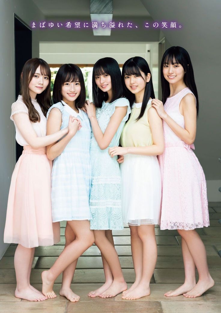 Five young women in pastel dresses standing barefoot indoors